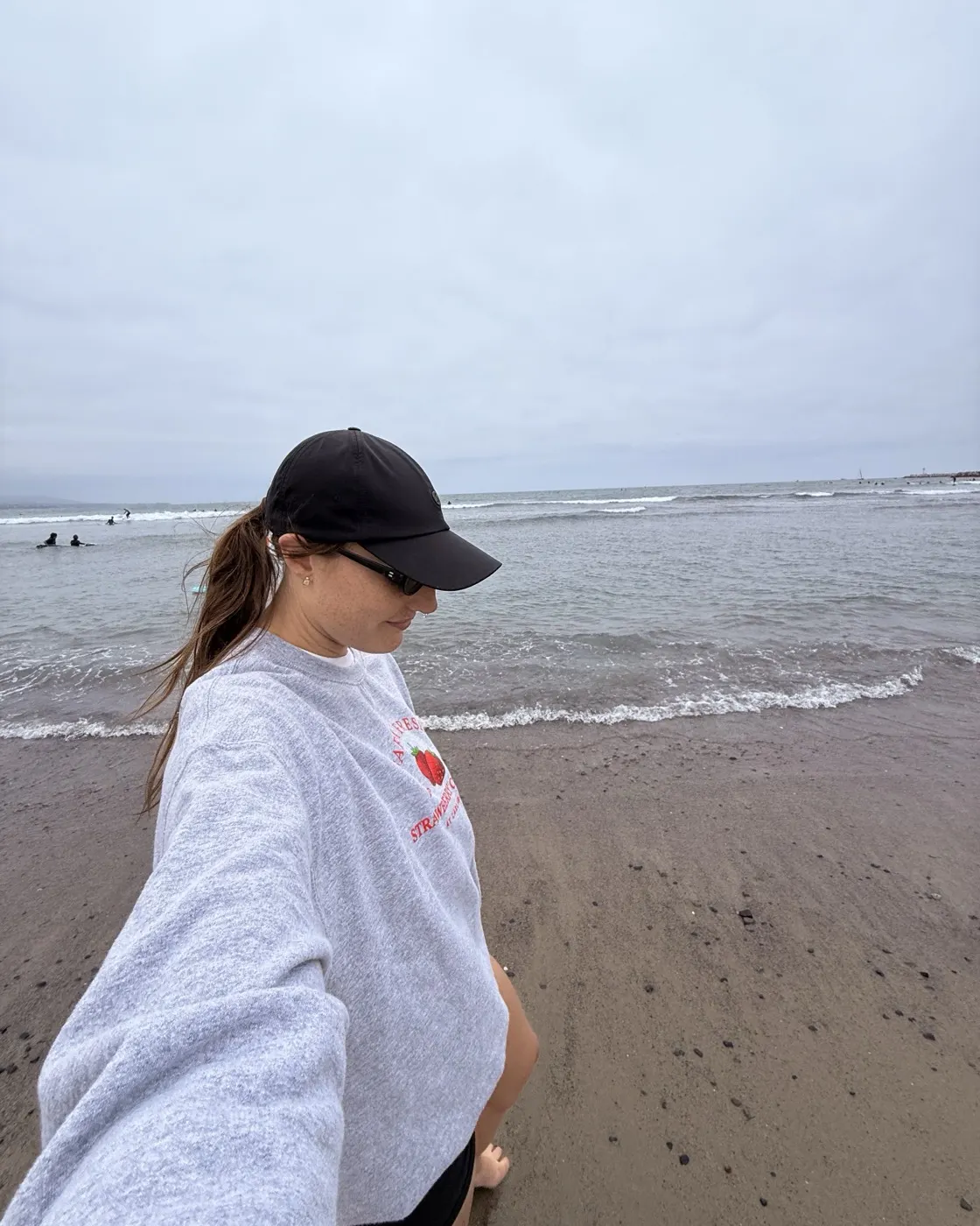 Kylie walking on the beach in a grey sweatshirt and a black cap
